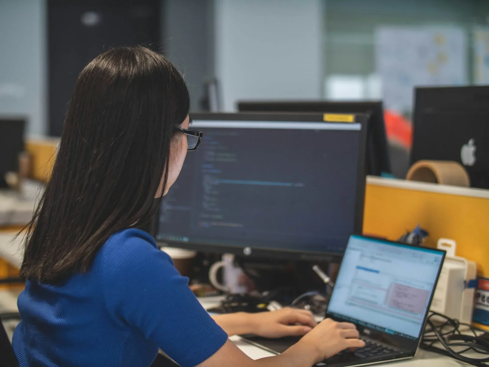 Asian IT professional at a dual-monitor workstation managing Microsoft 365